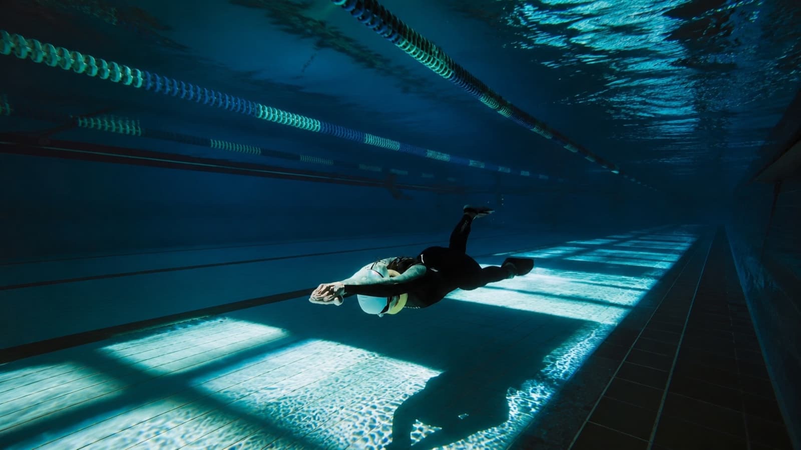 A freediver with fins swimming below the pool surface